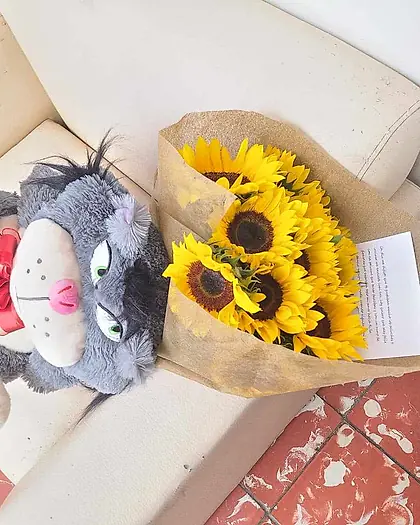 Ramo de girasoles acompañado de peluches sobre un sofá claro